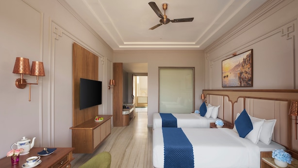 A hotel room with two beds, a TV, a desk with a chair, and a painting on the wall.