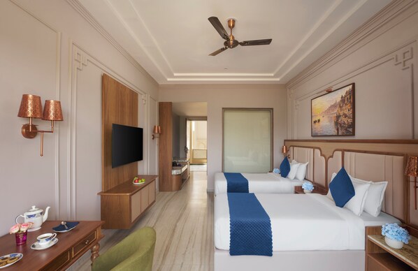 A hotel room with two beds, a TV, a desk with a chair, and a painting on the wall.