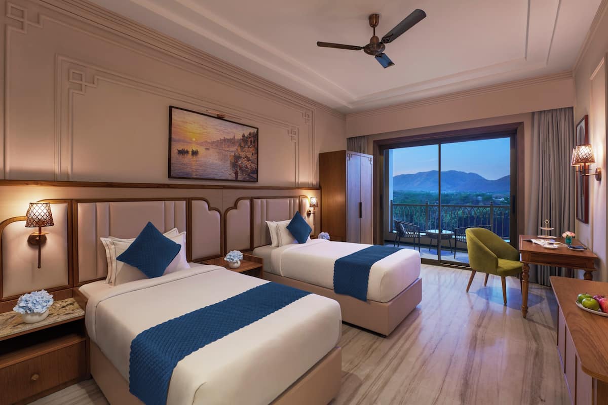 A hotel room with two beds, a desk, a chair, a TV, and a balcony with a mountain view.