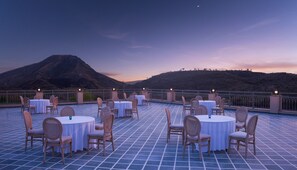 Eine Terrasse mit runden Tischen und Stühlen, einem Fliesenboden und einer Bergkulisse.