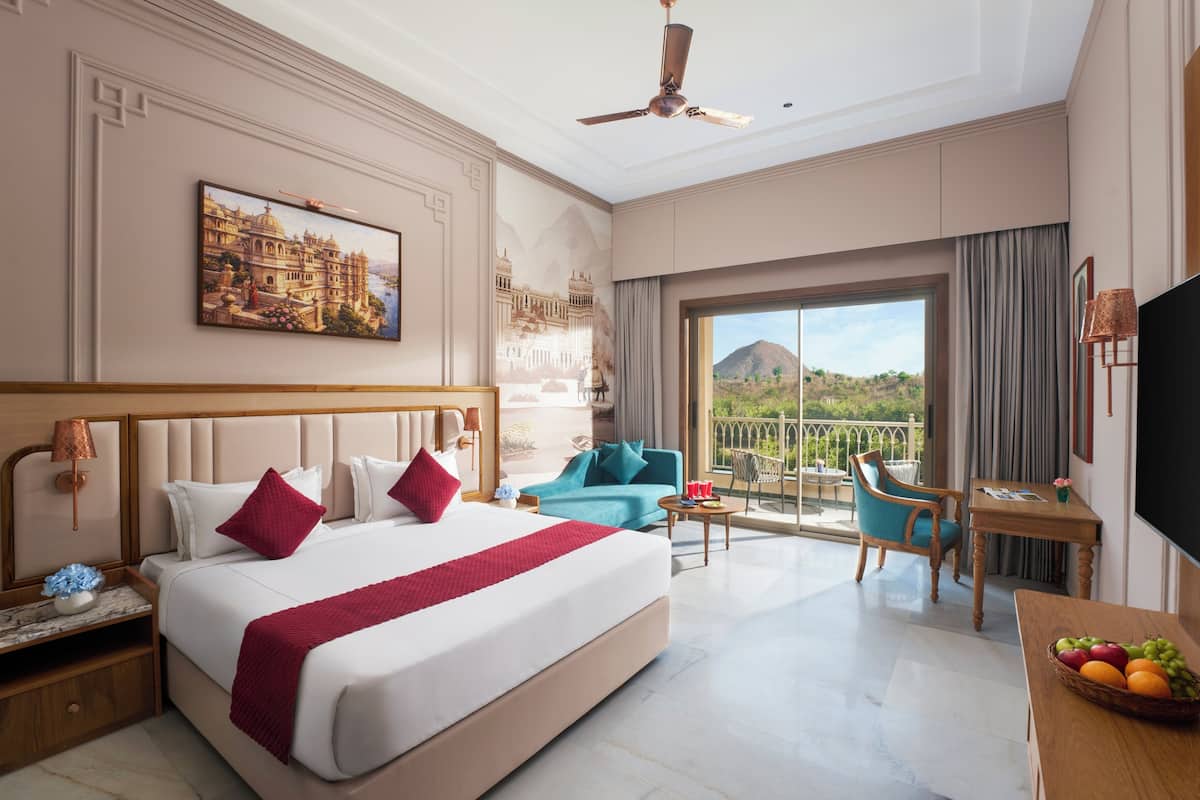 A hotel room with a large bed, a balcony with a view, a desk with a lamp, and a television.