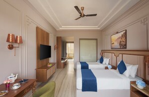 A hotel room with two beds, a TV, a desk with a chair, and a ceiling fan.