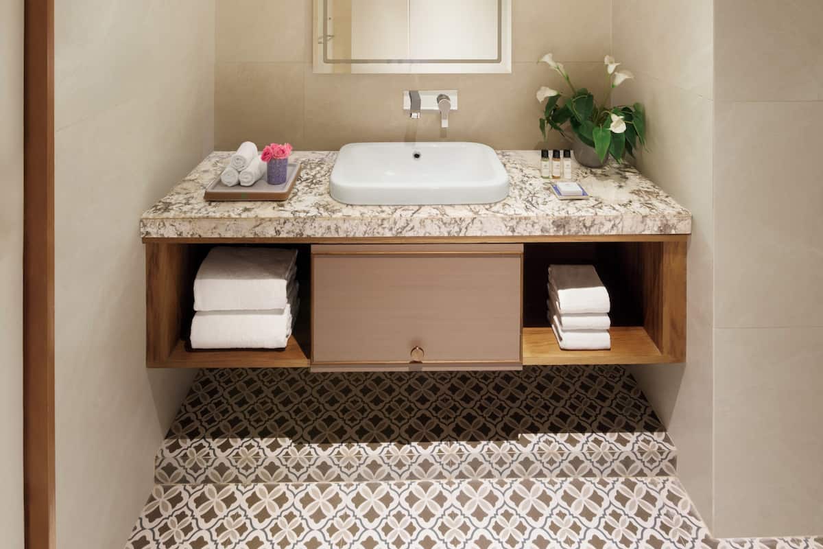 A bathroom with a marble sink, a mirror, a towel rack, and patterned floor tiles.