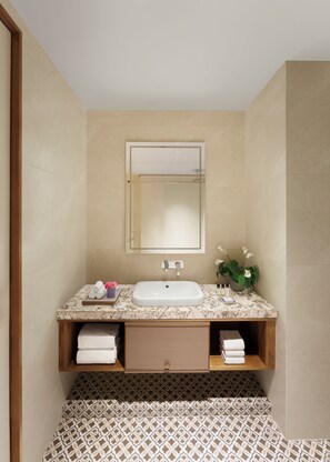 A bathroom with a marble sink, a mirror, a towel rack, and patterned floor tiles.