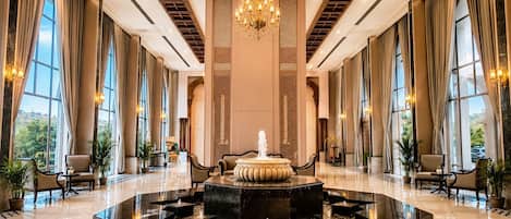 A spacious lobby with a central fountain, large windows, and elegant chandeliers.