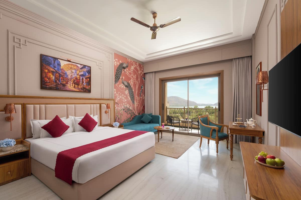 A hotel room with a bed, a sofa, a desk, a chair, a TV, and a balcony with a view.