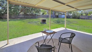 Eine überdachte Terrasse mit Tisch, Stühlen, einem Grill und einem Rasen.