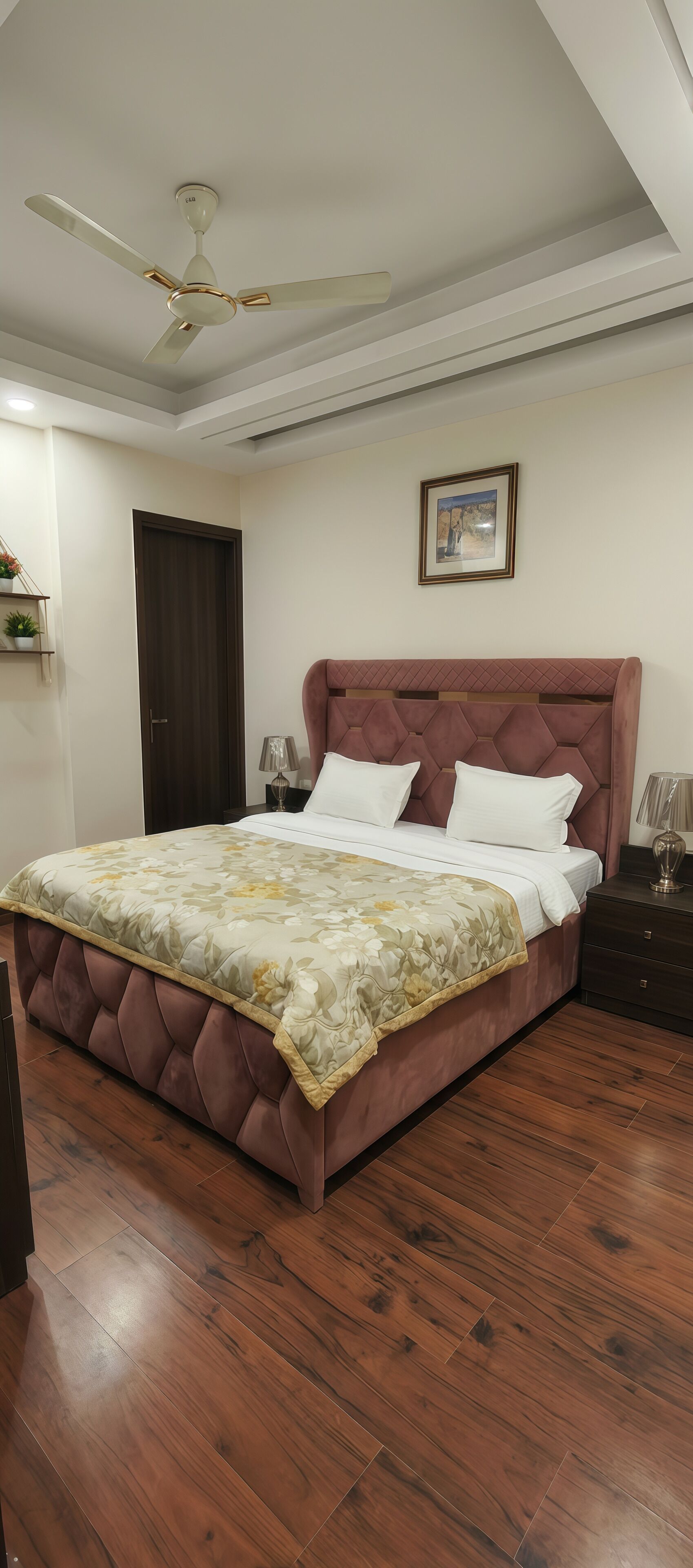A bedroom with a bed, a ceiling fan, a framed picture on the wall, and a nightstand with a lamp.