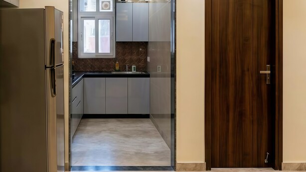 A modern kitchen with a refrigerator, cabinets, and a wooden door.