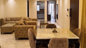 A spacious living area with a large L-shaped sofa, a dining table with chairs, and a kitchen in the background.