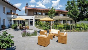 Ein modernes Gebäude mit einer Terrassenfläche, die Gartenmöbel und Sonnenschirme beinhaltet, umgeben von Grünflächen.