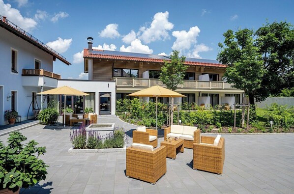 Un bâtiment moderne doté d’un patio aménagé avec du mobilier d’extérieur et des parasols, le tout entouré de verdure.