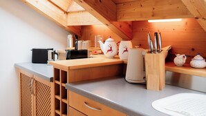 Eine kleine Küche mit Holzausstattung, einer Arbeitsplatte und verschiedenen Küchenutensilien, darunter ein Teekessel, Tassen und ein Messerblock.