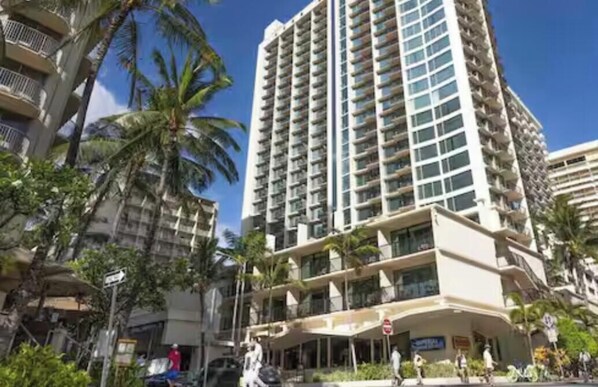 A high-rise hotel with multiple balconies, palm trees, and a clear blue sky. - Cozy 1-bedroom condo one short block from the beach! (Honolulu)