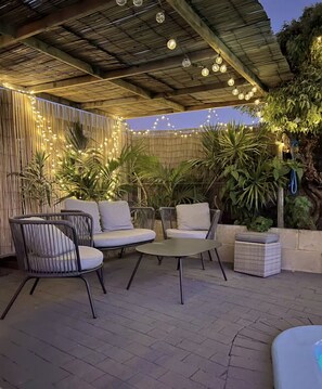 An outdoor patio with wicker furniture, string lights, and potted plants.