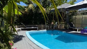 Una piscina con solárium empedrado, sillas de descanso y sombrillas.