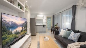 Una sala moderna con una televisión de pantalla plana, un sofá, una mesa de centro y una cocina al fondo.