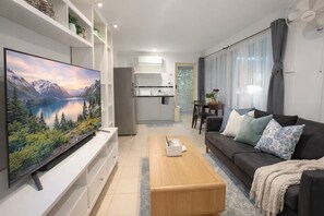 A modern living room with a flat-screen TV, a sofa, a coffee table, and a kitchen in the background.