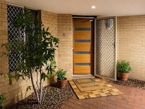 A modern entrance with a wooden door, a welcome mat, and potted plants. - Perth Beach House (Mullaloo)