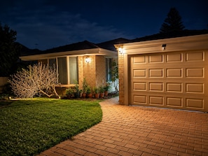A residential garage with a brick pathway leading to it, surrounded by a well-maintained lawn and potted plants.