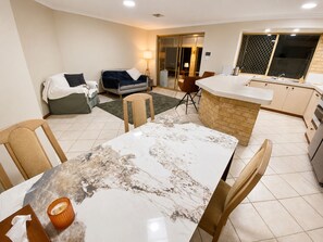 A modern kitchen with a marble countertop, a dining area with a marble table, and a living space with a sofa and a lamp. - Perth Beach House (Mullaloo)