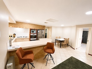 A compact kitchen with a dining area, featuring a brick backsplash, modern appliances, and a small bar area.