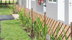 Un hotel con fachada gris, varios balcones con plantas colgantes, una valla de madera y un extintor montado en la pared.