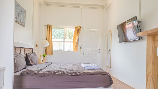 Un dormitorio con cama, ventana con cortinas, televisor montado en la pared y una puerta.