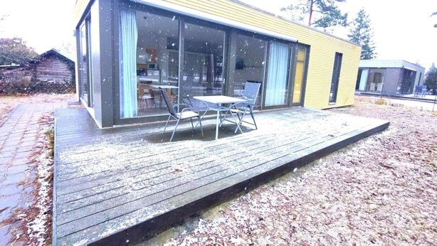 Uma casa moderna com varanda, janelas amplas e área de jantar com mobiliário externo.