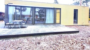 Um edifício moderno com grandes janelas de vidro, telhado plano e área de pátio com mobiliário externo.