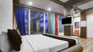 A bedroom with a bed, curtains, a TV, and a sliding door to a balcony.