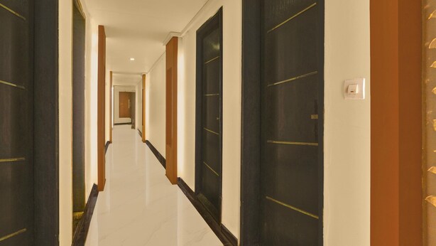 A hotel hallway with dark doors, a white floor, and a light switch on the wall. - Collection O Lodha Experia Mall (Kalyan)