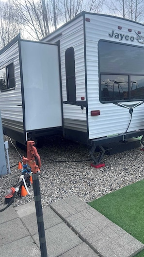 A Jayco RV with a sliding door, a window, and a visible water hose. - Waters Riverfront Property,Pets OK, Fully Fenced (Cascade)