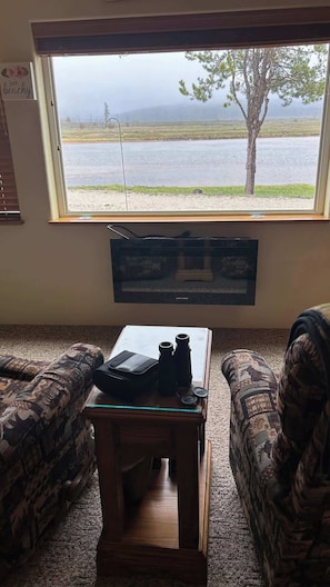 A room with a large window overlooking a body of water, a television mounted on the wall, and a small wooden table with a remote control. - Waters Riverfront Property,Pets OK, Fully Fenced (Cascade)