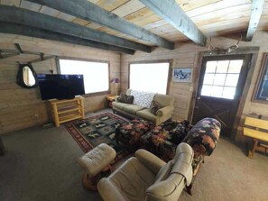 A rustic cabin interior with a wooden ceiling, a television, a sofa, a patterned rug, and a bench. - The Perfect Cozy Cabin of Elo Road! (McCall)