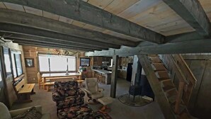 Een rustiek interieur met houten balkenplafond, een zithoek, een eethoek en een wenteltrap.