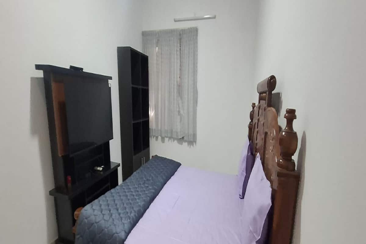 A bedroom with a bed, a TV stand, a wardrobe, and a window with curtains.