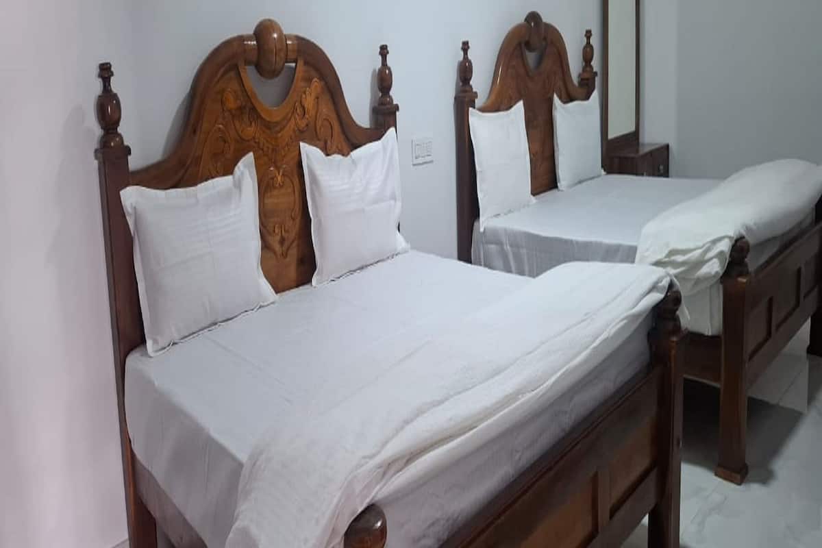 Two wooden beds with white linens in a room with white walls and a tiled floor.