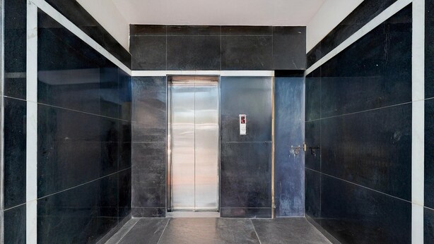 A modern elevator with a metallic finish, surrounded by dark tiled walls and a clean floor. - Super Collection O Electronic City (Anekal)