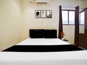 A hotel room with a bed, a window with curtains, and three framed pictures on the wall.
