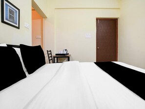 A hotel room with a bed, a small table with a kettle, and a door.