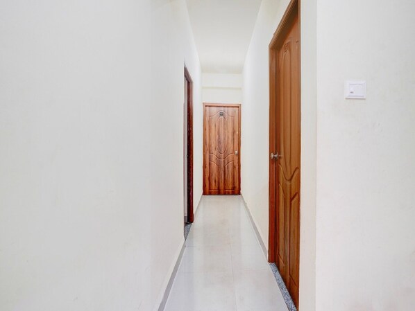 A narrow hallway with white walls and a tiled floor, leading to a wooden door at the end.