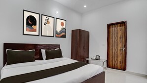 A neatly arranged bedroom with a bed, a wardrobe, a small table with a kettle, and framed artwork on the wall. - Super Hotel O SGT University Road (Gurugram)