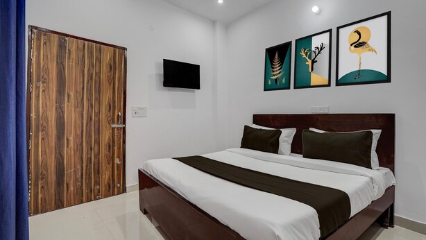 A bedroom with a wooden door, a bed with white and dark bedding, and three framed artworks on the wall. - Super Hotel O SGT University Road (Gurugram)
