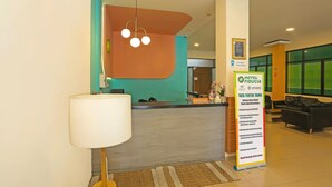 Uma área de recepção de hotel com balcão, placa indicativa, espaço de espera e um sofá.