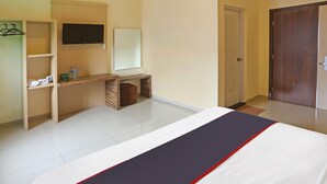 Quarto de hotel com cama, escrivaninha, cadeira, televisão e guarda-roupa.