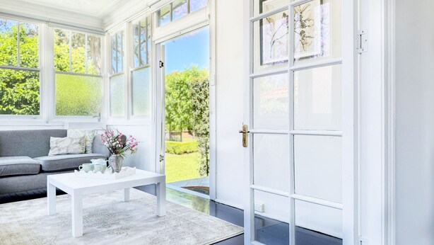 Una habitación luminosa con una puerta blanca, un sofá gris y una mesa de centro blanca.
