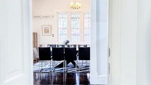 Comedor con una mesa dispuesta para cuatro, sillas, una araña y un ventanal con vidrieras.