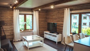 A log cabin interior with a television, white furniture, and large windows. - Klaukse in Kolga-Aabla: Only 40 min. from Tallinn, sandy beach in 10 min. on foot. (Kolga-Aabla)
