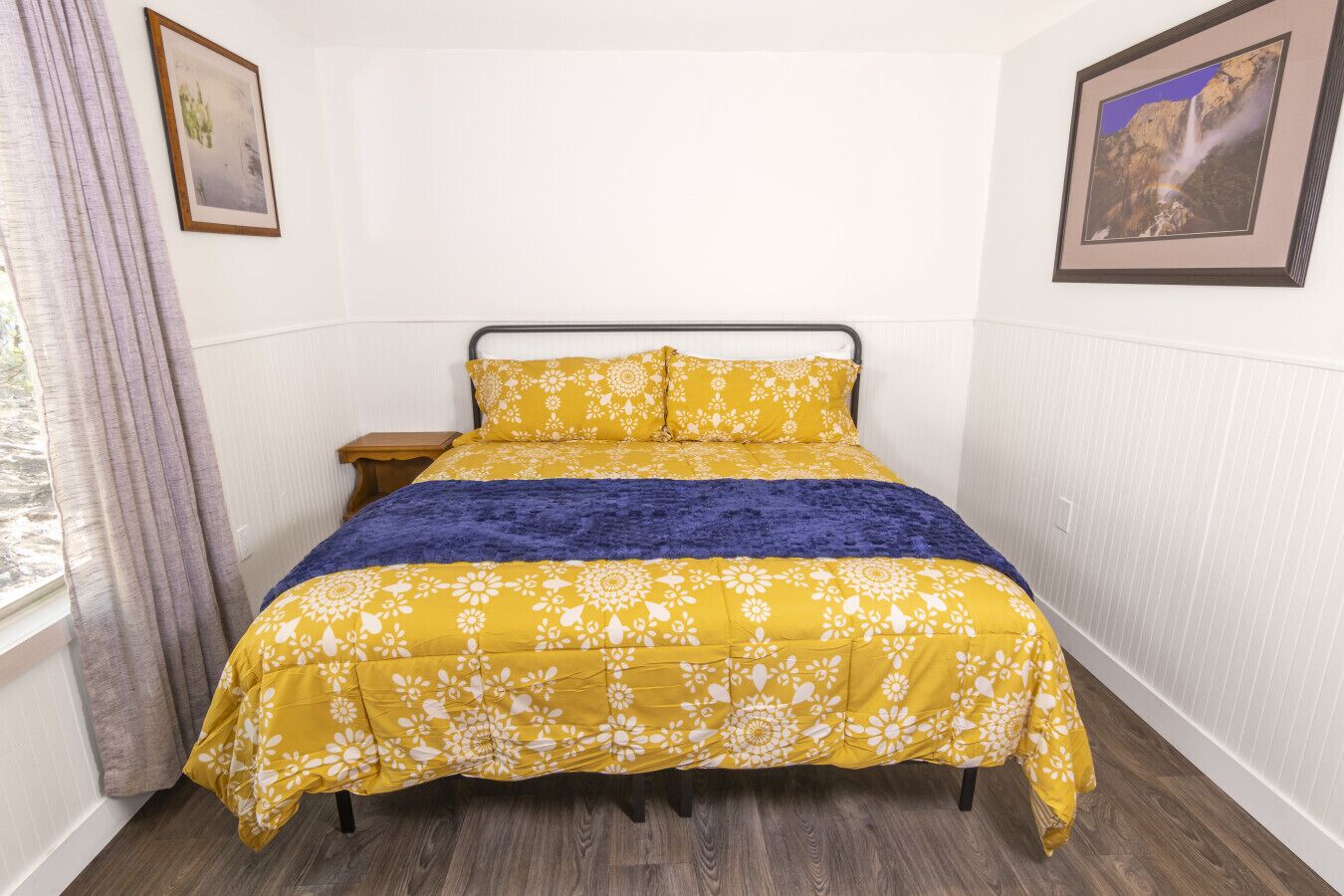 A bed with a floral bedspread, a dark blue throw blanket, and a wooden headboard.